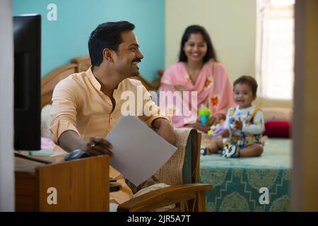 Vater arbeitet zu Hause, während Mutter mit ihrem Baby auf dem Bett spielt Stockfoto