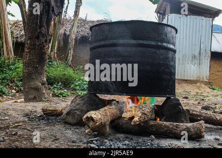 Ein Topf auf einem Holzfeuer, das für die handwerkliche Herstellung von Palmöl verwendet wird, in der Landessprache „Seketa“ (Stir) genannt, unter dem Regen von Frauen des Dorfes Mpety in Walikale in Nord-Kivu (östlichen DR Kongo), 15. Dezember 2021. Une marmite sur un feu de bois servant à la Fabrication artisanale de l’huile de palme appelee en langue locale „Seketa“ (Remuer) sous la pluie par des femmes du Village Mpety a Walikale au Nord Kivu (Est de la RD Congo), am 15. Dezember 2021. Stockfoto