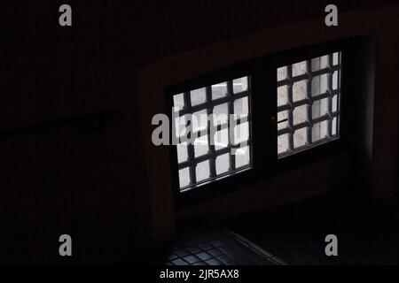 Dunkles Zimmer mit Fenster im Gitter. In der Gefängniszelle . Leicht, hoher Kontrast Stockfoto