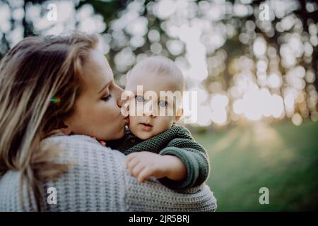 Mutter hält ihren kleinen Sohn im Strickpullover während des Spaziergangs in der Natur. Stockfoto