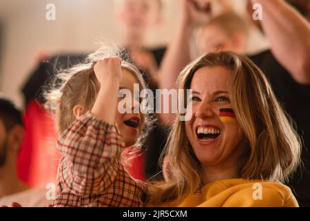 Begeisterte Fußballfans, Mutter mit kleiner Tochter, die die deutsche Nationalmannschaft in einem Live-Fußballspiel im Stadion unternahmen. Stockfoto