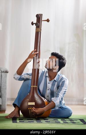 Porträt eines jungen Musikers, der zu Hause seine Tanpura stimmt Stockfoto