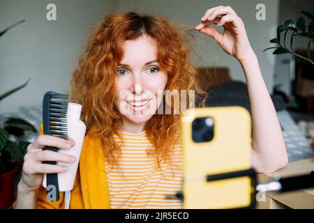 Rothaarige Bloggerin sendet Live-Bewertungen von Schönheitsprodukten für Haare Stockfoto