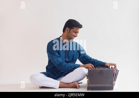 Porträt eines fröhlichen jungen Mannes, der Harmonium spielt Stockfoto