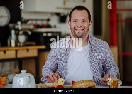 Unabhängiger Mann mit Down-Syndrom, der das Frühstück in seiner Wohnung vorbereitet. Stockfoto
