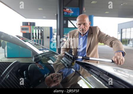 Leitender Geschäftsmann, der an der Tankstelle Autofenster waschen kann. Stockfoto