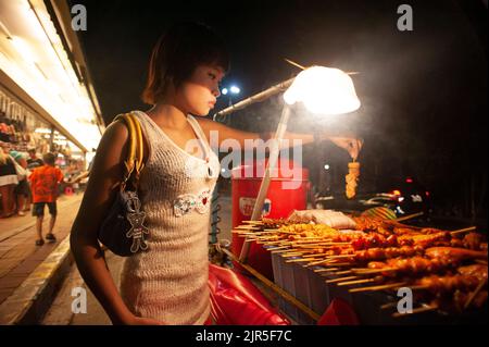 Pattaya, Chon Buri, Thailand - 24. Juni 2011: Thai-Mädchen mit moderner Kleidung, die in den Straßen von Pattaya einen Fleischsnack kaufen. Stockfoto