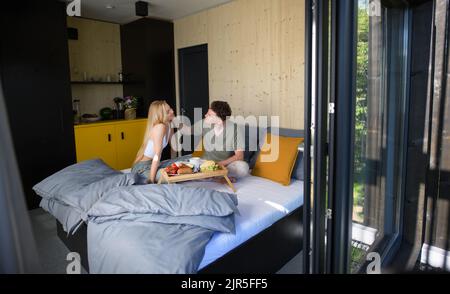 Junge schöne Paar in der Liebe sitzt im Bett und mit gesunden Frühstück zusammen. Stockfoto