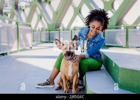 Multirassisches Mädchen, das mit ihrem Hund draußen auf der Brücke sitzt und sich ausruht, ihn trainiert und gemeinsam Freizeit verbringt. Konzept der Beziehung zwischen Stockfoto