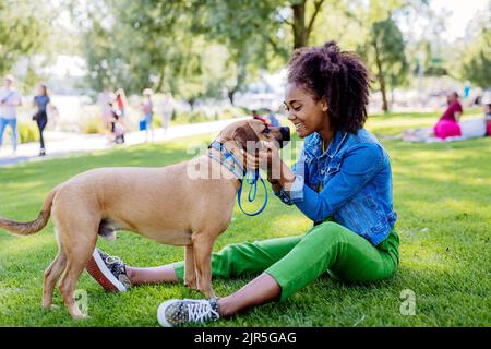 Multirassisches Mädchen, das mit ihrem Hund draußen im Park sitzt und sich ausruht, ihn trainiert und gemeinsam Freizeit verbringt. Konzept der Beziehung zwischen Stockfoto