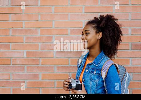 Multirassisches Teenager-Mädchen mit Rucksack und Skateboard, vor der Stadtmauer. Stockfoto