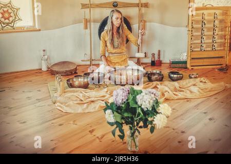 Schöne Frau spielt auf tibetischer Schale, zeremonieller Raum. Stockfoto