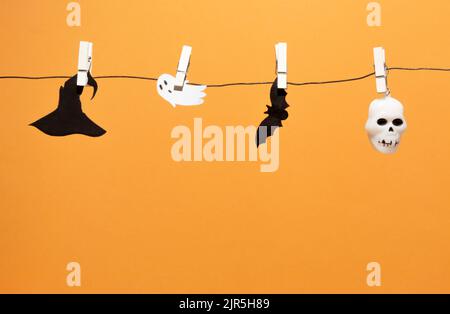 Fledermaus Silhouette, Schädel, Geist und Hexenhut auf Wäscheleine mit Wäscheklammern. Orangefarbener Hintergrund mit Kopierbereich. Trendige Halloween Hintergrund. Stockfoto