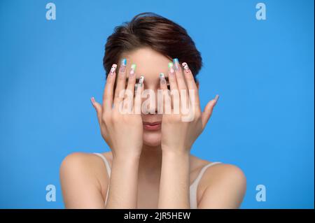 Skinny Teenager-Mädchen nettes Mädchen versteckt ihr Gesicht in ihren Händen auf blauem Hintergrund Stockfoto