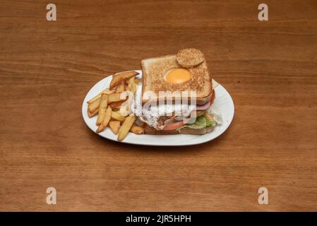 Ein köstliches und befriedigendes extremes Sandwich mit einem Spiegelei mit Eigelb, Salat, Tomaten und yorkschinken und hausgemachten Pommes frites Stockfoto