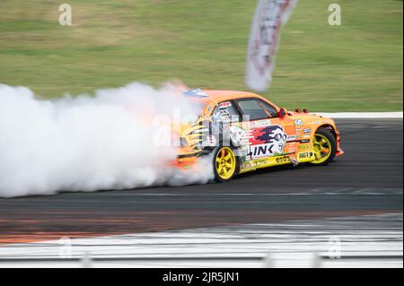 Ein orangefarbener BMW E36, der Rauch auf einer Spur für einen Driftwettbewerb erzeugt Stockfoto