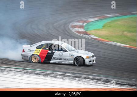 Ein grauer BMW E46 mit den deutschen Flaggenfarben, der auf einer Spur Rauch für einen Driftwettbewerb erzeugt Stockfoto