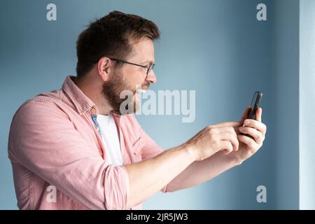 Profil eines fröhlichen lächelnden Mannes, der ein Smartphone in den Händen hält und online über Videokommunikation kommuniziert. Stockfoto
