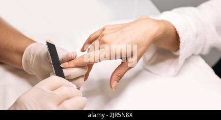 Manikuristin feilt Frauennägel an ihren Arbeitstisch. Nagelpflege-Prozess, Nahaufnahme Stockfoto