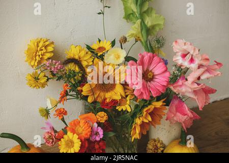 Herbst florales Stillleben, stimmungsvolles Bild. Bunte Herbstblumen, Kürbisse, Pattypan zerquetscht Komposition gegen rustikale Wand. Ernte in Ländern Stockfoto