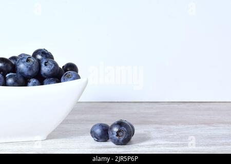 Eine Nahaufnahme einer Schale mit Heidelbeeren auf einem Tisch vor weißem Wandhintergrund Stockfoto