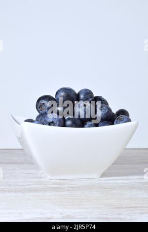 Eine vertikale Aufnahme einer Schale mit Heidelbeeren auf einem Tisch vor weißem Wandhintergrund Stockfoto