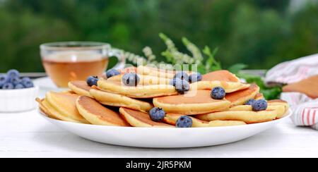 Amerikanische Pfannkuchen in einer weißen Schüssel mit frischen Heidelbeeren, eine Tasse Tee zum Frühstück. Banner, Nahaufnahme Stockfoto