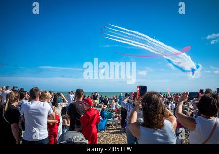 Die Menschen beobachten das RAF Red Arrows Kunstflugteam vom Strand aus bei der jährlichen Eastbourne Airshow in East Sussex, Großbritannien. Stockfoto