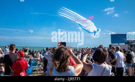 Die Menschen beobachten das RAF Red Arrows Kunstflugteam vom Strand aus bei der jährlichen Eastbourne Airshow in East Sussex, Großbritannien. Stockfoto