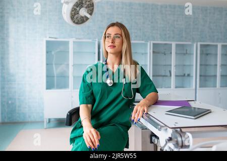 Eine Ärztin in einem OP-Anzug im Krankenhaus, mit einer Maske, die wegschaut. Stockfoto