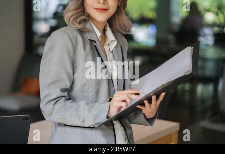 Junge schöne asiatische Unternehmen Frau halten Papier Konto Dokumente informelle Tabelle Finanzbuchhalter Beratung Arbeit Stand Überprüfung Bericht Stockfoto