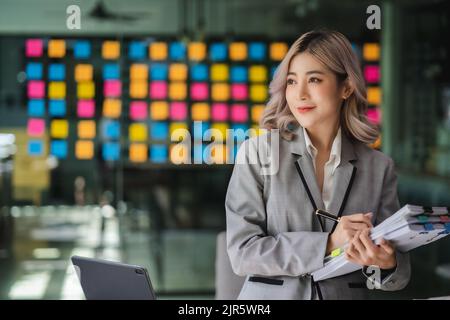 Junge schöne asiatische Unternehmen Frau halten Papier Konto Dokumente informelle Tabelle Finanzbuchhalter Beratung Arbeit Stand Überprüfung Bericht Stockfoto