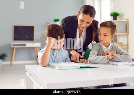 Die fürsorgliche Lehrerin hilft kleinen Schülern, das Lesen zu lernen und erklärt Unterrichtsmaterial. Stockfoto