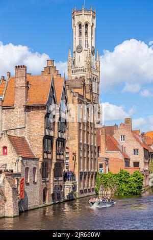 Touristen genießen eine geführte Bootsfahrt um die Kanäle von Brügge, Belgien - vorbei am Relais Bourgondisch Cruyce Hotel mit dem Belfried von Brügge (Belfor Stockfoto