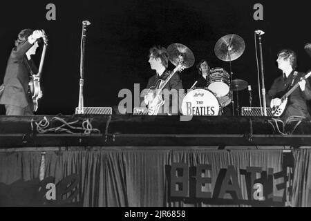 Die Beatles auf der Bühne beim Gator Bowl in Jacksonville, Florida, am 11. September 1964. Hurrikan Dora hatte Jacksonville am Vortag getroffen, und die verbleibenden starken Winde, die auf 45 mph zustürmen, erforderten, dass Ringo Starr's Trommeln auf die Bühne genagelt wurden und dass der Pappschriftzug der Beatles auf der Seite der Bühne schließlich weggerissen wurde. (USA) Stockfoto