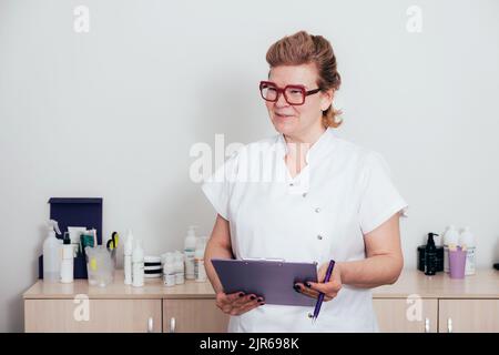 Ein Arzt im weißen Mantel lächelt und hält ein Notizbuch in den Händen Stockfoto