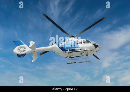 Blau-weißer Rettungshubschrauber für Rettungswagen, der mitten in der Luft vor einem blauen Himmel fliegt Stockfoto