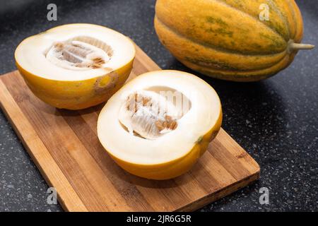 Hausgemachte gelbe reife Melone wird auf einem Holzbrett in zwei Hälften geschnitten. Ernte Melonen. Stockfoto