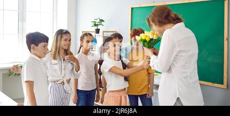 Niedliche Schüler mit Blumen für ihre beste Lehrerin in der Schule zu Ehren des Urlaubs. Stockfoto