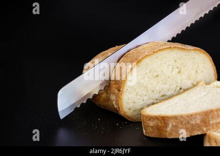 Messer schneiden frisch gebackenen Laib Brot. Nahaufnahme Metall Küchenmesser schneidet Brot auf Schneidebrett Stockfoto