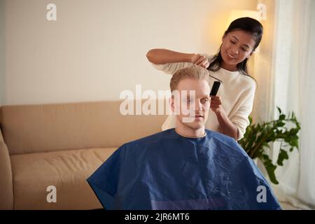 Lächelnde junge Frau, die im Rollstuhl Haare von ihrem Freund schneidet Stockfoto