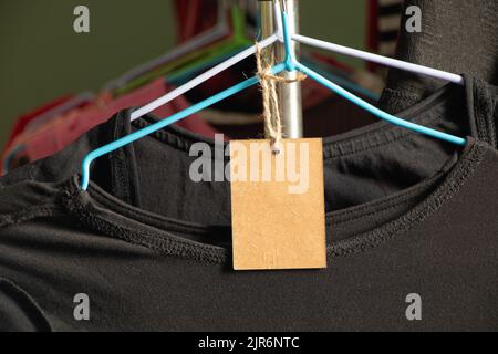 Karton, Verpackung, lässig, Kleidung, Branding, Shopping, braunes Papier Preisschild wiegt auf Kleidung auf einem Rack auf einem Kleiderbügel im Verkaufsbereich, blank pri Stockfoto