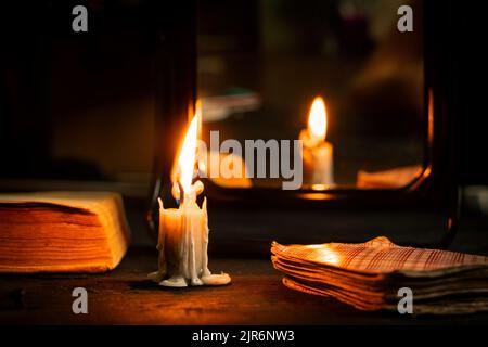 Eine brennende Kerze wurde von Spiegeln getragen und Wahrsagerkarten liegen in der Nähe, Wahrsagerei auf Karten bei Kerzenlicht auf einem schwarzen Tisch, Magie, Hexe A Stockfoto