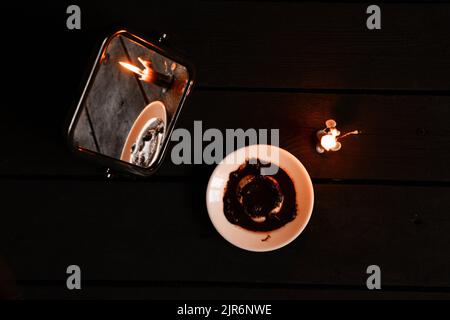 Eine brennende Kerze wurde von Spiegeln getragen und es gibt Wahrsagerkarten und Kaffeesatz auf einem Teller in der Nähe, Wahrsagerei auf Karten von Candleli Stockfoto