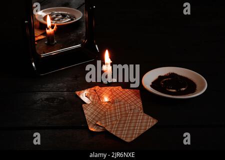 Eine brennende Kerze wurde von Spiegeln getragen und es gibt Wahrsagerkarten und Kaffeesatz auf einem Teller in der Nähe, Wahrsagerei auf Karten von Candleli Stockfoto