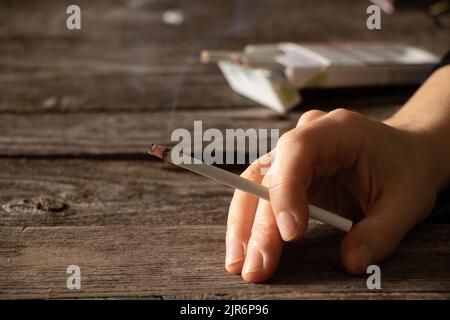 Frau, die eine Zigarette zu Hause am Tisch hält, im Dunkeln zu Hause raucht, Nikotin und schlechte Angewohnheit, Zigaretten und Krebs und Rauchen Stockfoto