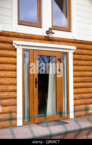 Eingangstür mit Fenstern und Beleuchtung in einem Holzhaus aus abgerundeten Stämmen. Stockfoto