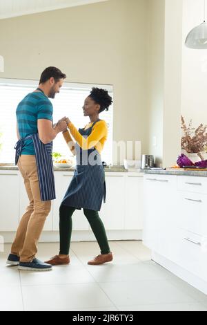 Vertikales Bild des glücklichen, vielfältigen Paares, das in der Küche tanzt Stockfoto