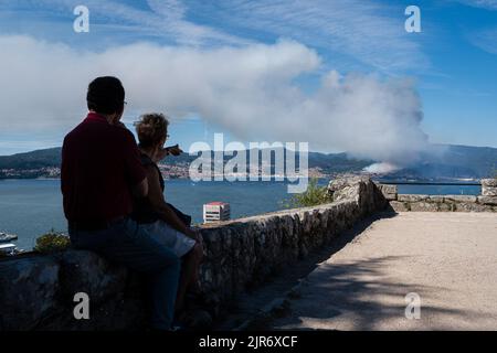 Zwei Personen beobachten den Rauch des Feuers in der Gemeinde Moaña von der Burg Castro in Vigo aus. Ein Waldbrand in der Nähe des Stadtgebiets der Gemeinde Moaña, Galizien, Spanien, kann von der Stadt Vigo aus gesehen werden. Das Feuer hat dazu geführt, dass Autobahnen abgeschnitten und Wohnungen geräumt wurden. Nach Angaben des spanischen Ministerium für den ökologischen Übergang haben die Brände im Land in diesem Jahr bisher mehr als 250.000 Hektar verbrannt. Eine alarmierende Zahl, wenn man bedenkt, dass der historische Rekord im Jahr 2012 mit 166.185,66 Hektar verbrannt wurde. Stockfoto