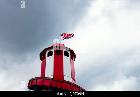 Sie blicken auf einen Helter Skelter mit einer Gewerkschaftsfahne, die oben gegen einen dunklen, wolkigen Himmel fliegt Stockfoto